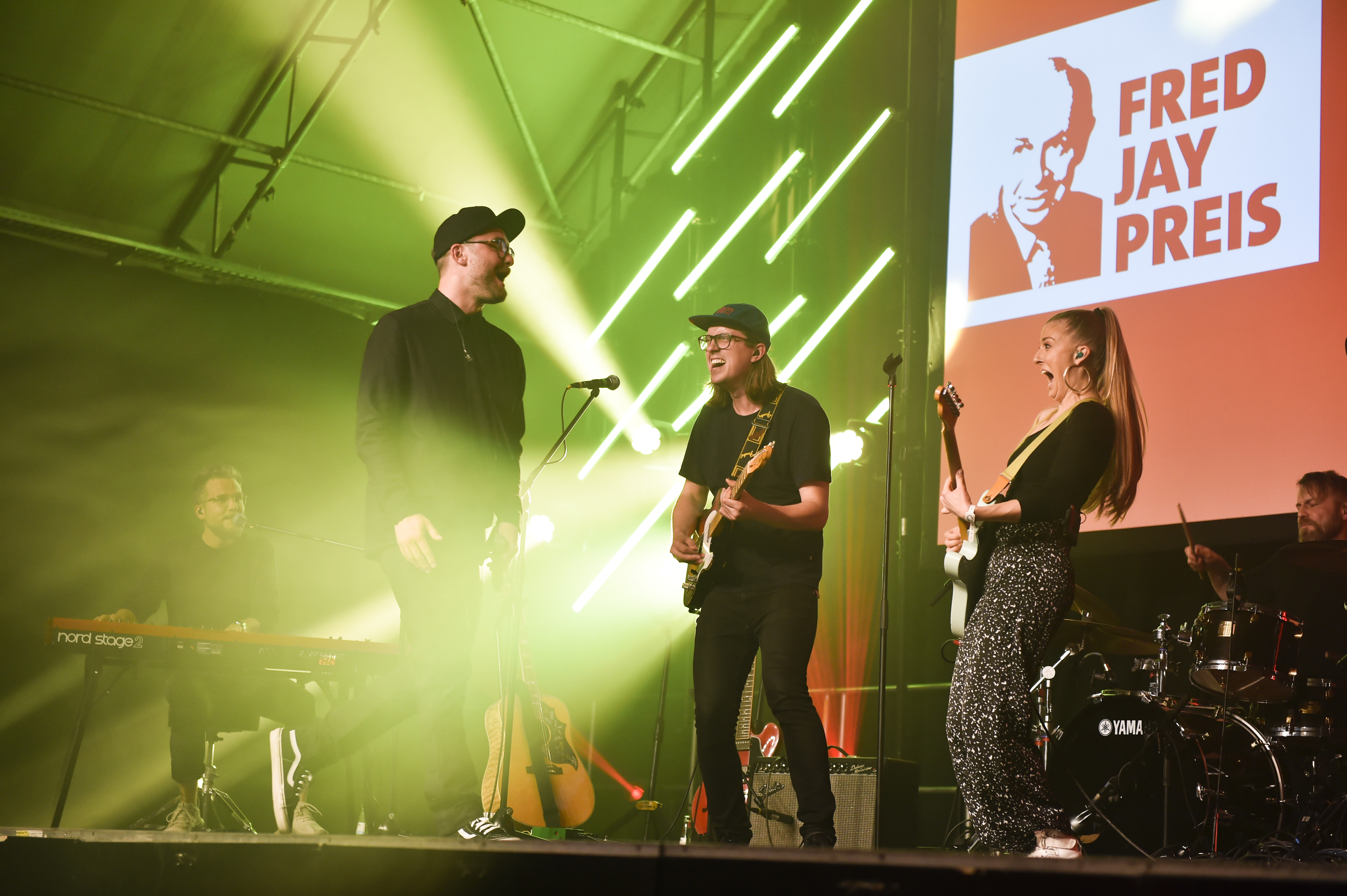 Vier Musiker spielen auf einer Bühne mit grünem Licht, im Hintergrund ein Fred Jay Preis Plakat.