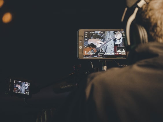 Ein Kameramann filmt einen Gitarristen, dessen Bild auf zwei Monitoren angezeigt wird.