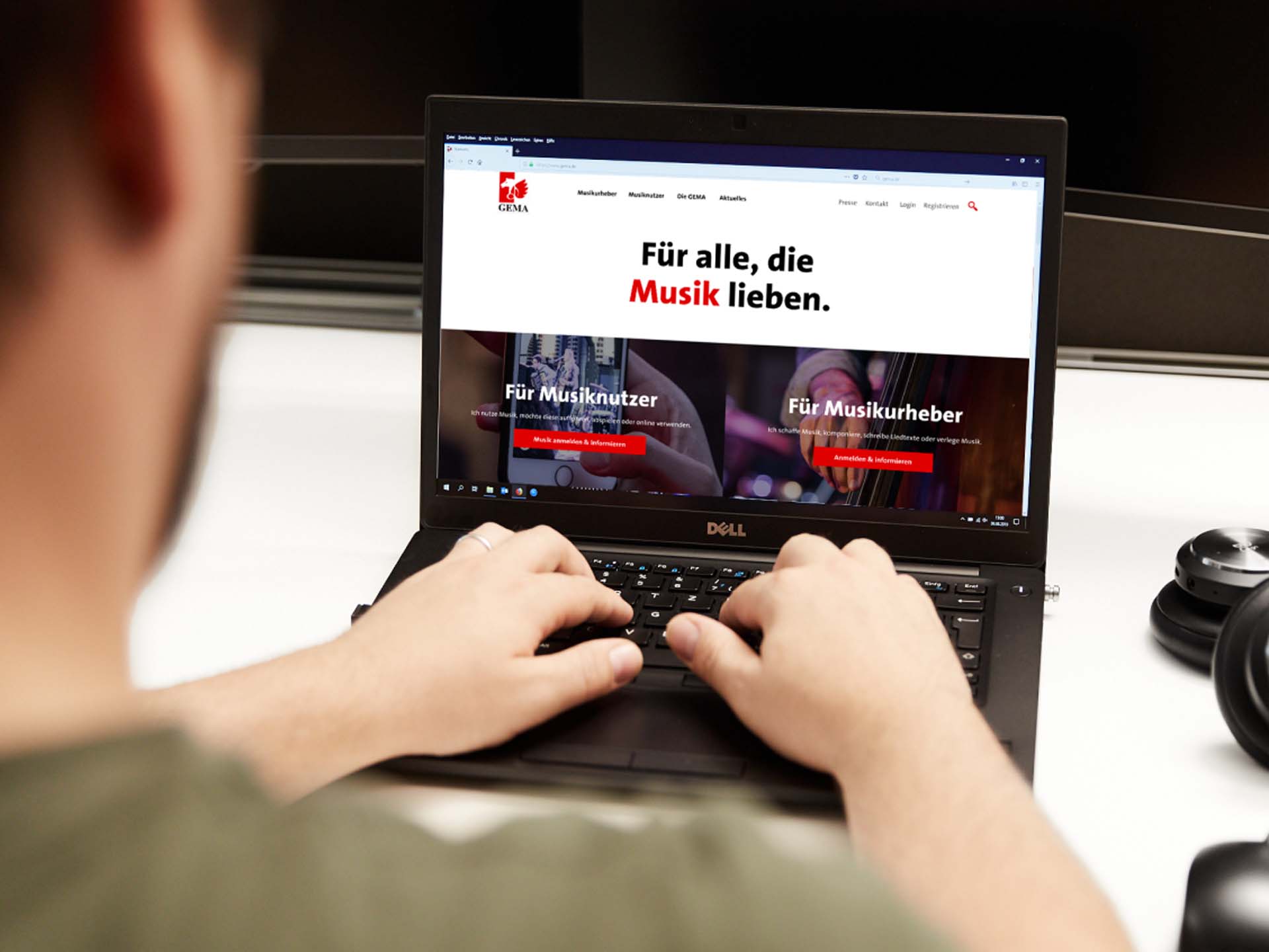 Eine Person tippt auf einem Laptop mit der GEMA-Website, umgeben von Kopfhörern.