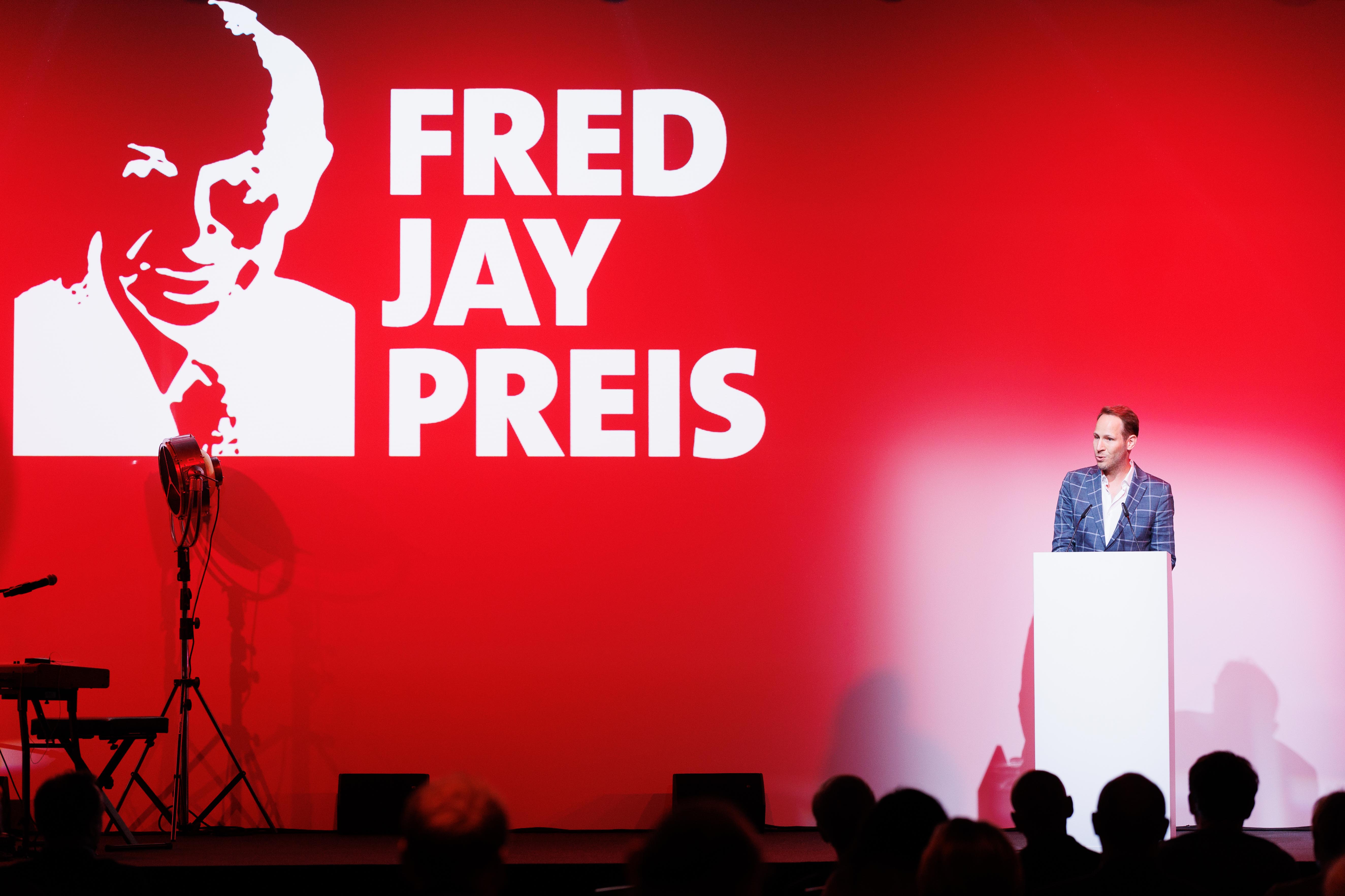 Mann am weißen Podium vor rotem Hintergrund mit