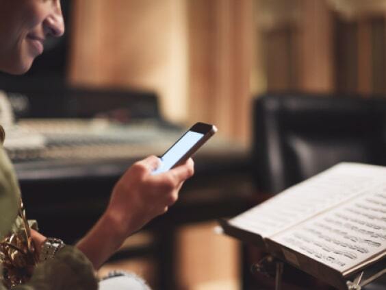 Person mit Smartphone in einem Musikstudio, hält ein Saxophon, Notenständer mit Noten im Vordergrund.