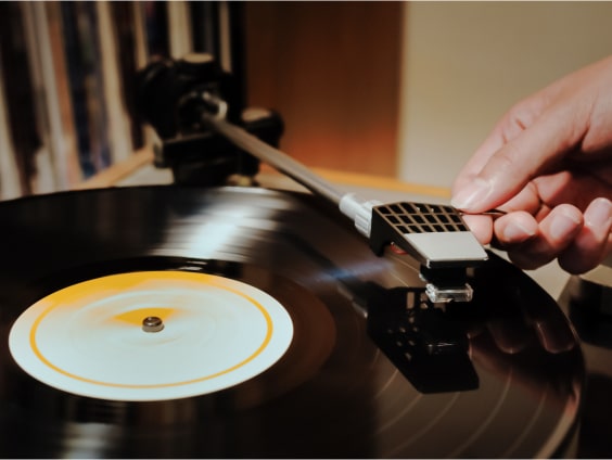 Eine Hand setzt den Tonarm auf eine schwarze Schallplatte mit weißem Etikett.
