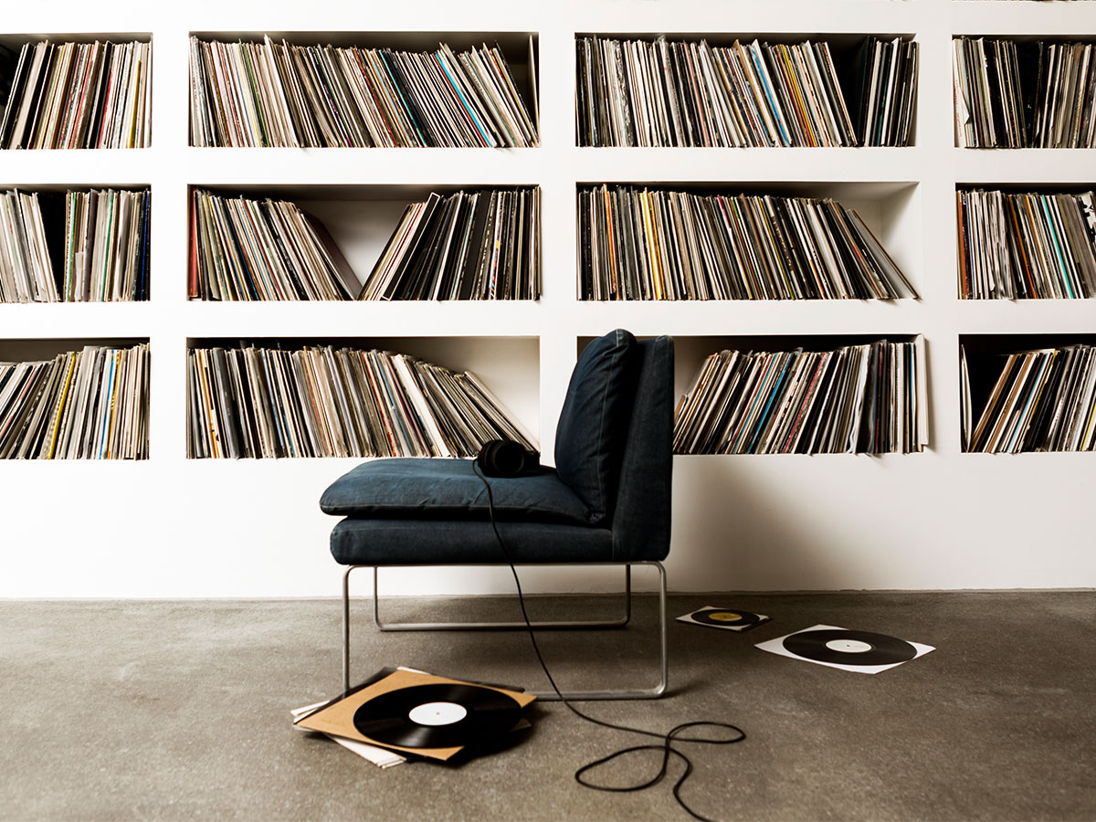 Ein Sessel vor einem Regal voller Schallplatten, mit Kopfhörern und Schallplatten auf dem Boden.