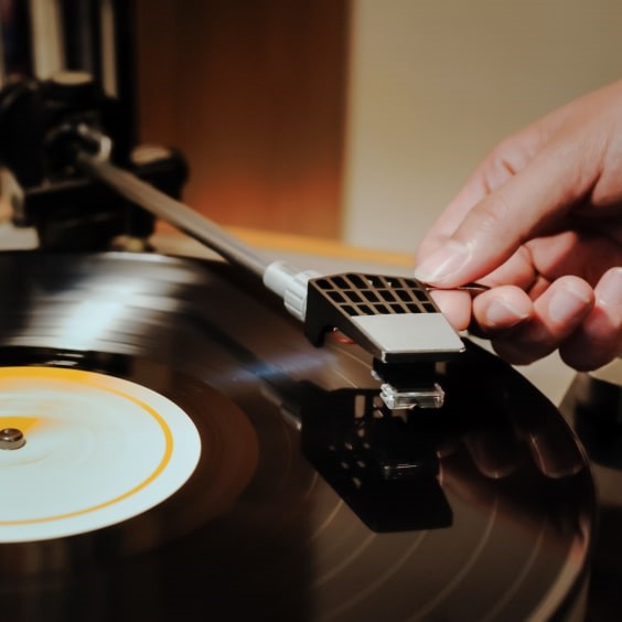 Hand hebt Tonarm auf schwarze Schallplatte mit gelbem Etikett.