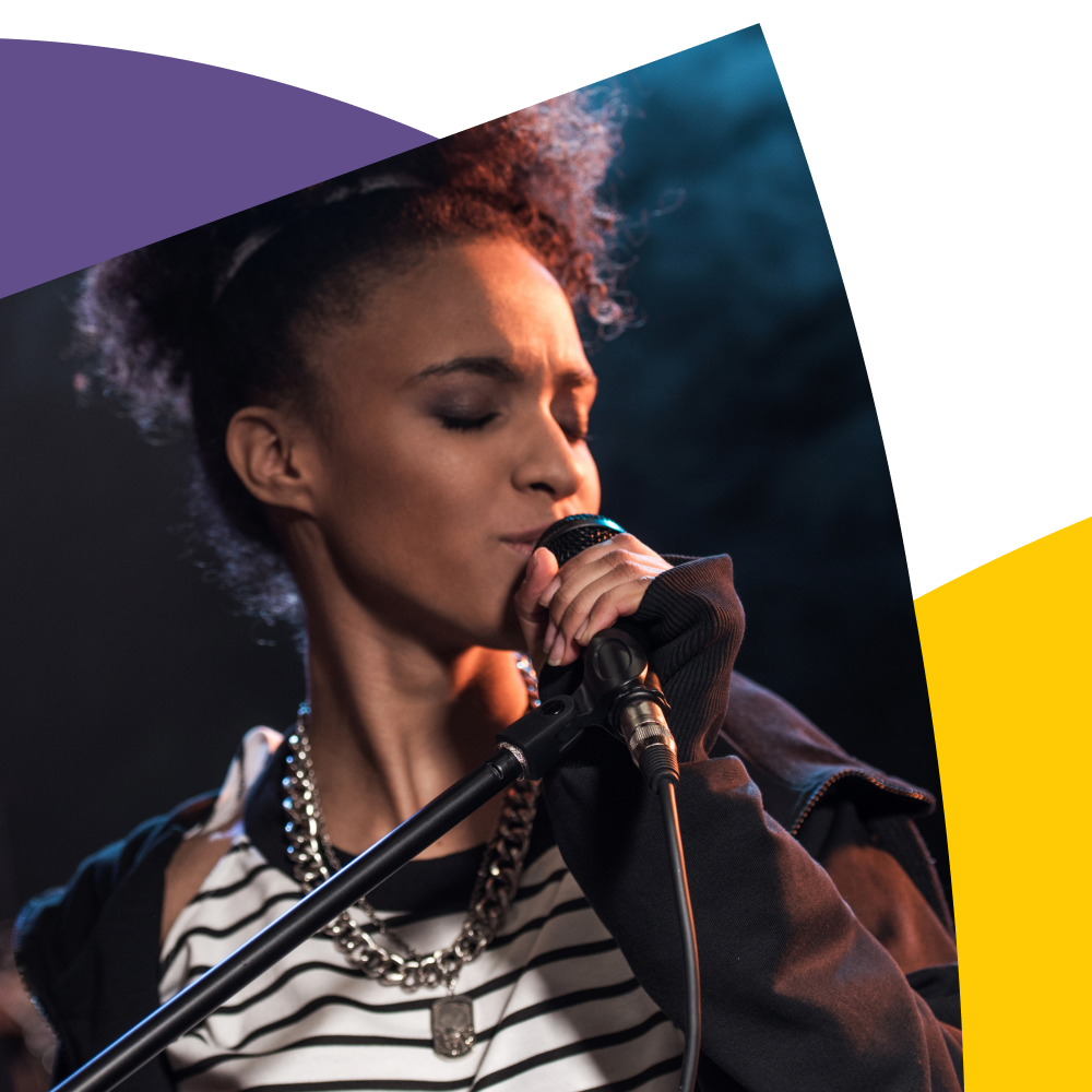 Eine Person singt leidenschaftlich in ein Mikrofon, vor einem dunklen Hintergrund.