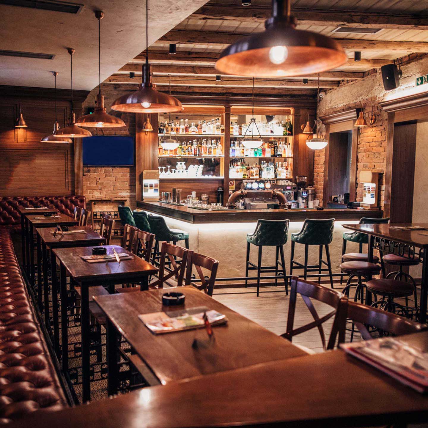 Eine gemütliche Bar mit Holztischen, Lederbänken und einer beleuchteten Theke voller Flaschen.