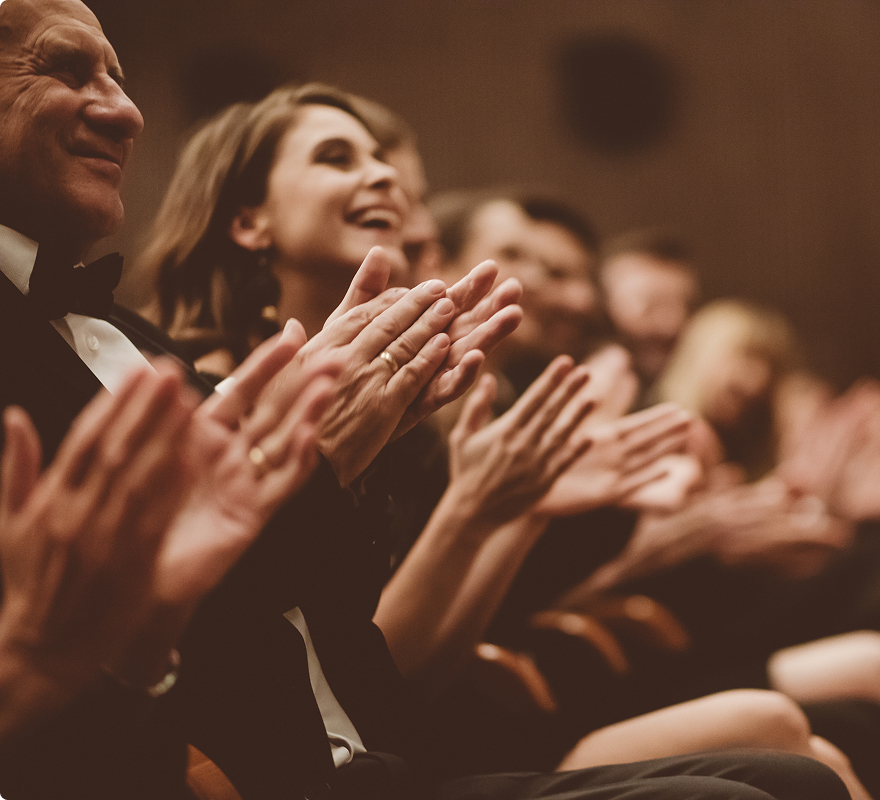 Menschen in Abendkleidung klatschen und lächeln in einem Theater oder Konzertsaal.