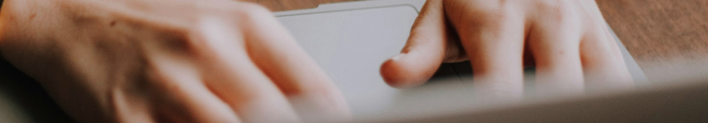 Hände tippen auf einem Laptop, Person trägt gelben Pullover und Armreif.