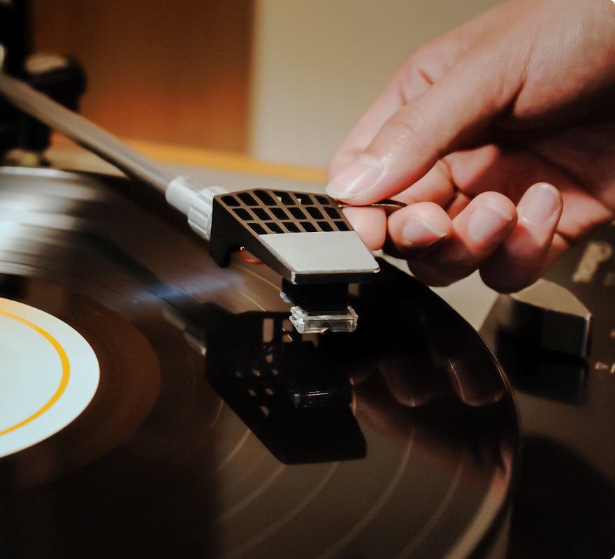 Eine Hand senkt den Tonarm auf eine schwarze Schallplatte.