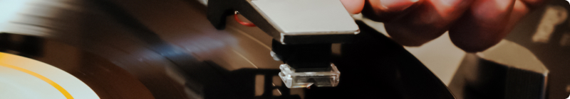 Eine Hand senkt den Tonarm auf eine schwarze Schallplatte.