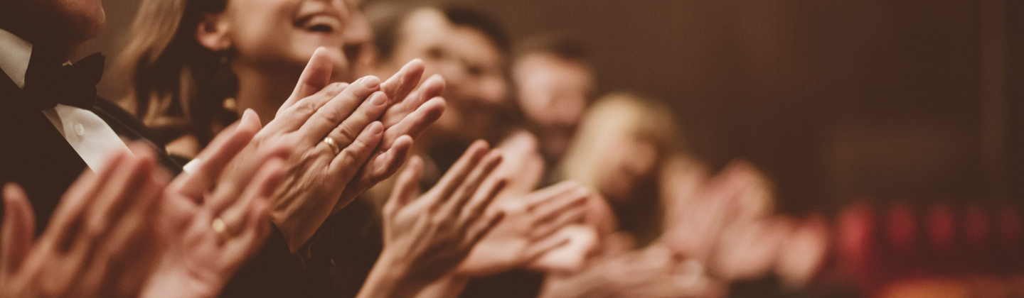 Menschen in Abendkleidung klatschen und lächeln in einem Theater oder Konzertsaal.