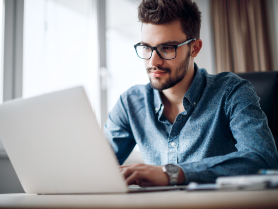 Ein Mann mit Brille arbeitet konzentriert an einem Laptop in einem hellen Raum.