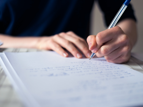 Eine Hand schreibt mit einem blauen Stift auf weißem Papier.