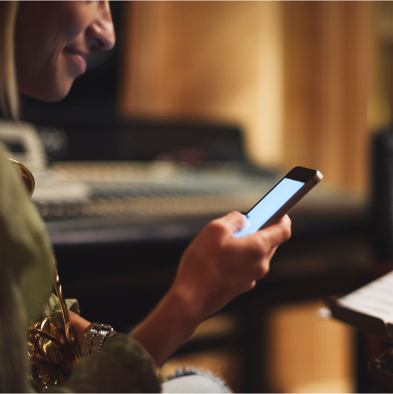 Person hält ein Smartphone und lächelt, im Hintergrund ein Mischpult.