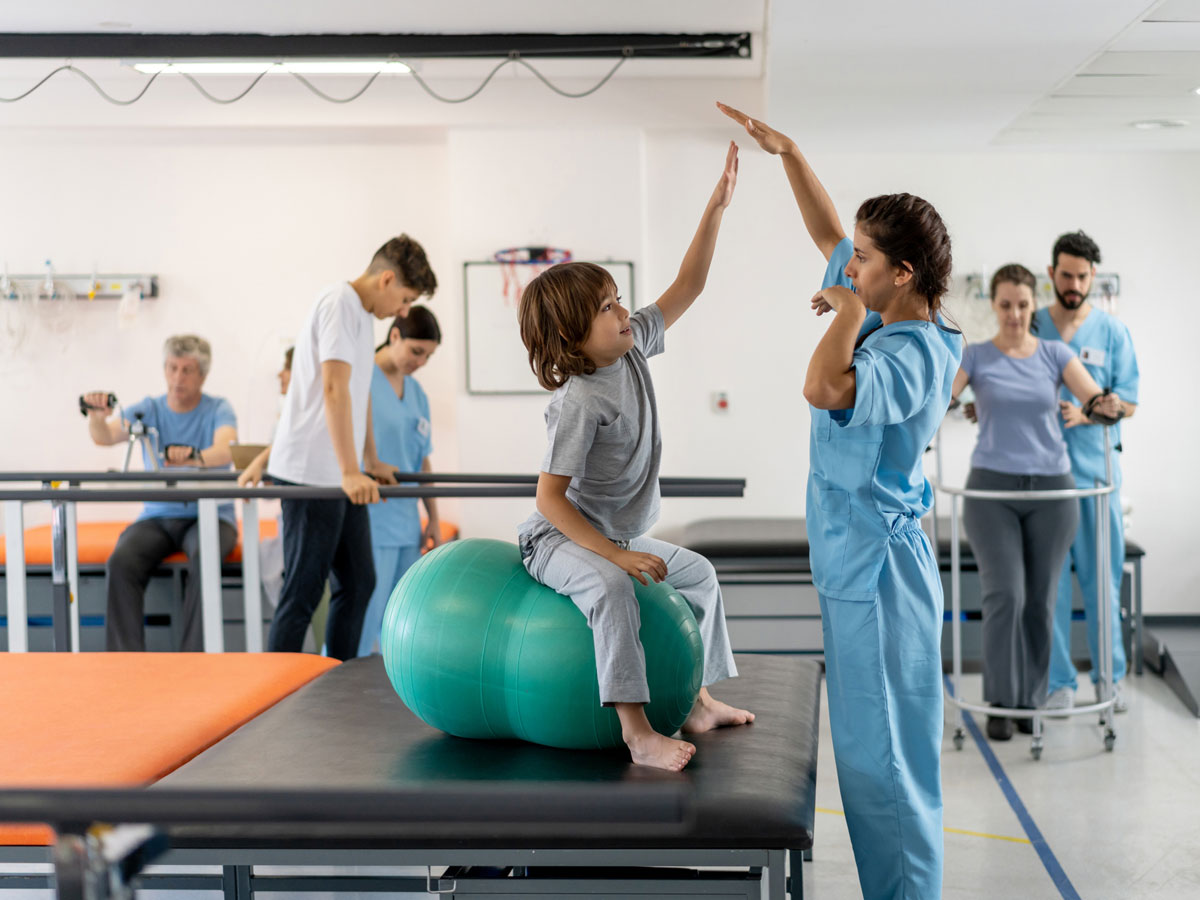 Ein Kind und eine Pflegerin bei der Krankengymnastik im Krankenhaus