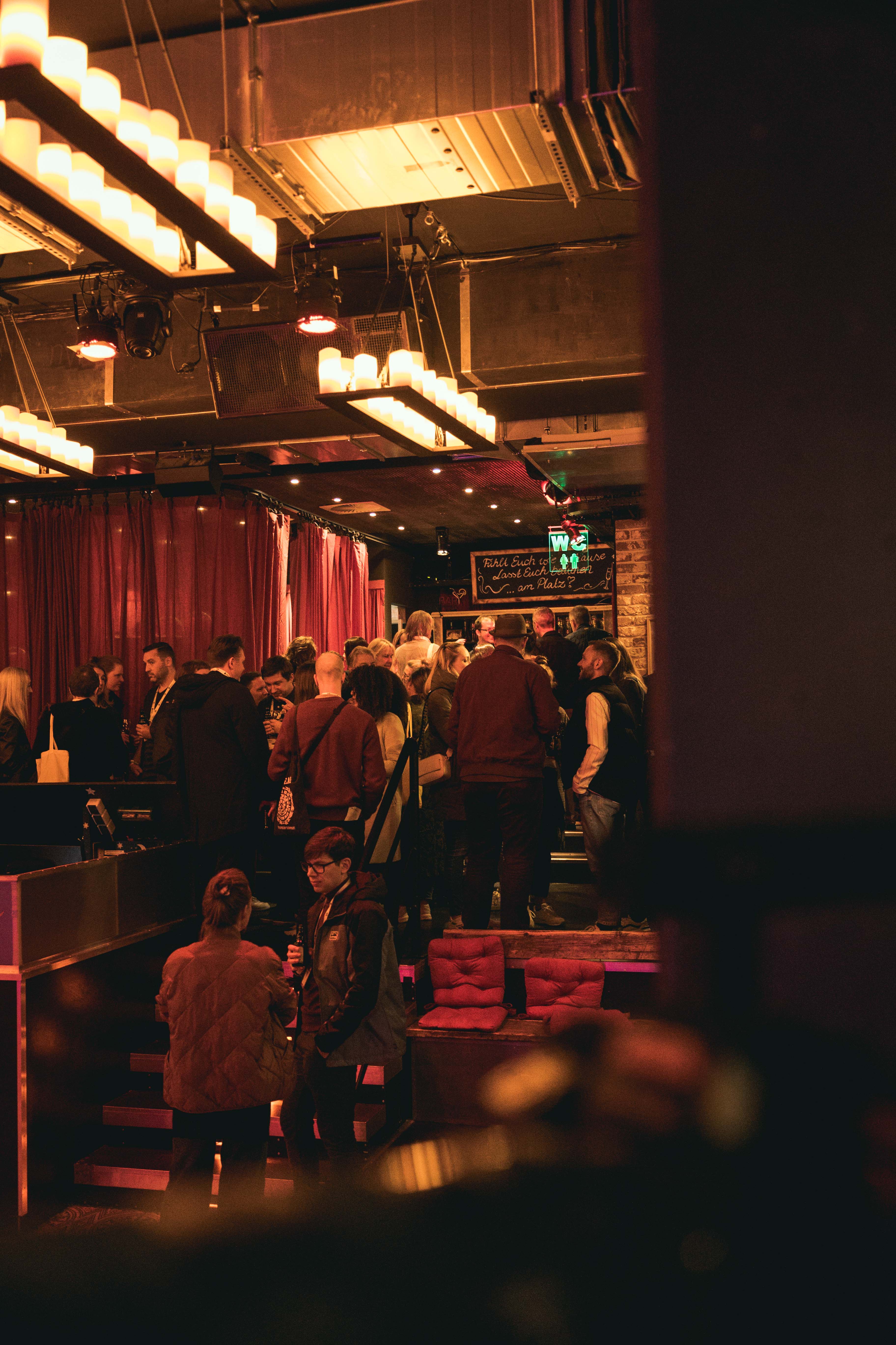 Menschenmenge in einer stimmungsvoll beleuchteten Bar mit roten Vorhängen und hängenden Lichtern.