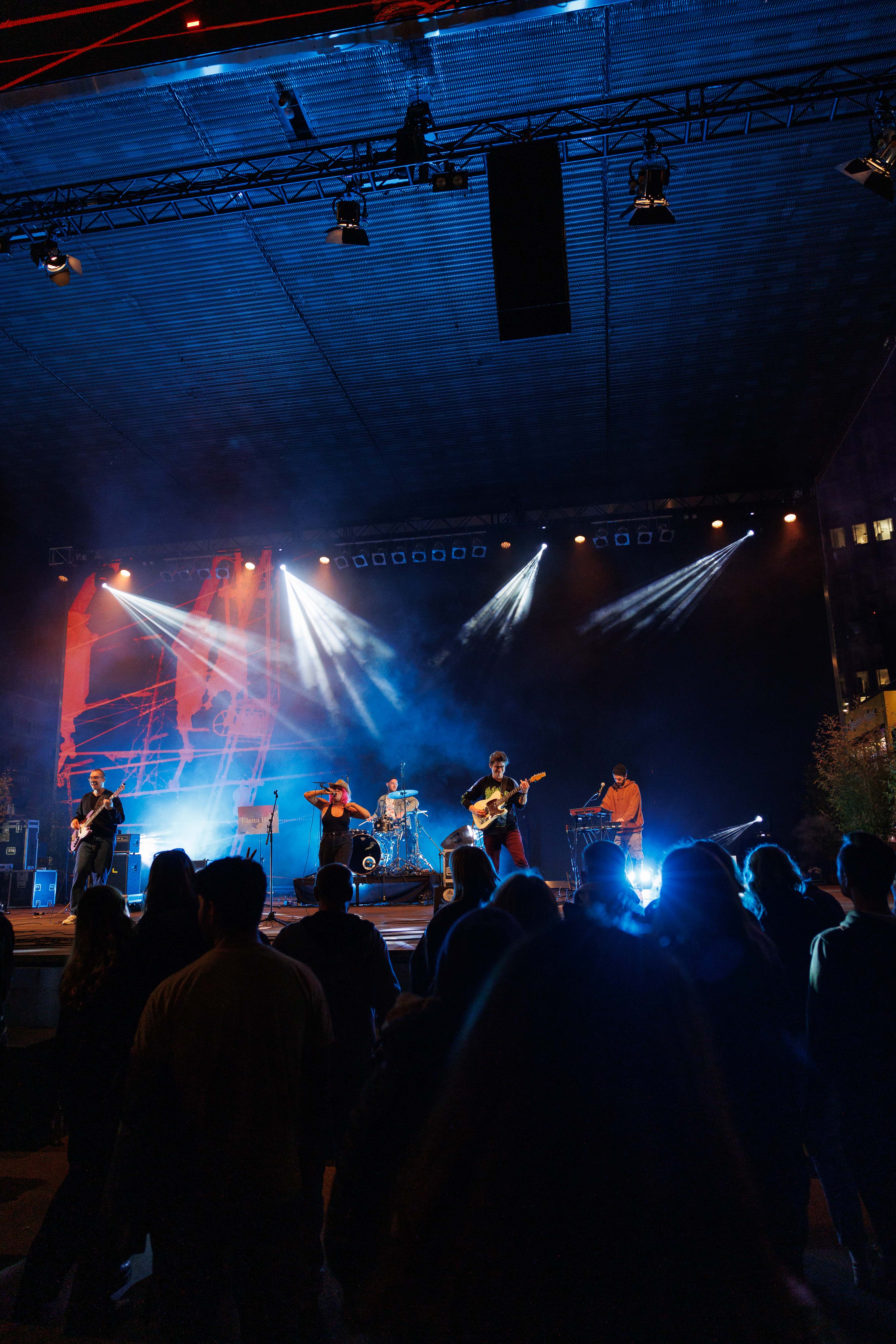 Eine Band spielt auf einer beleuchteten Bühne vor einem Publikum bei Nacht.