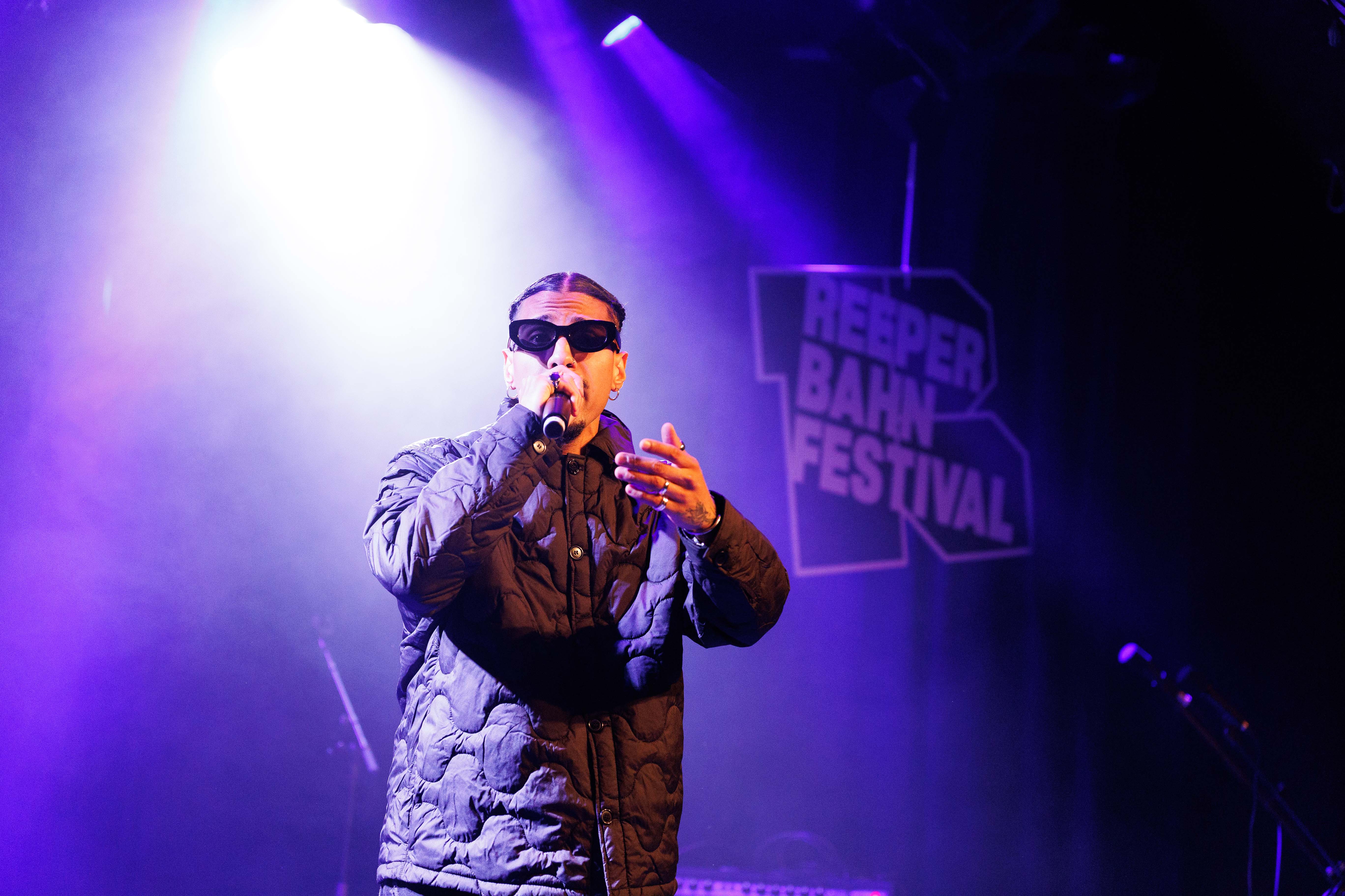 Ein Sänger mit Sonnenbrille performt auf der Bühne beim Reeperbahn Festival, beleuchtet von lila Scheinwerfern.