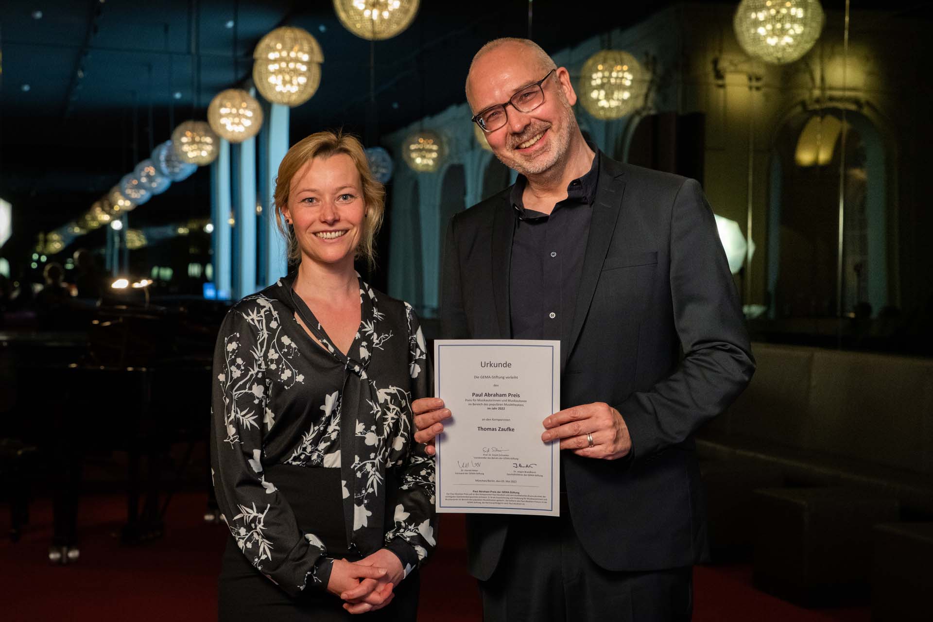 Zwei Personen lächeln, eine hält eine Urkunde