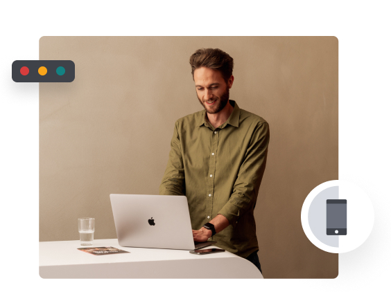 Ein Mann steht lächelnd an einem Tisch mit Laptop, Glas Wasser und Broschüre.