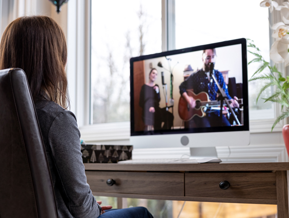 Eine Frau sitzt am Schreibtisch und schaut ein Konzert auf einem Computerbildschirm.