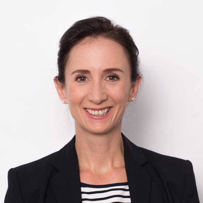 Eine lächelnde Person in schwarzem Blazer vor weißem Hintergrund.