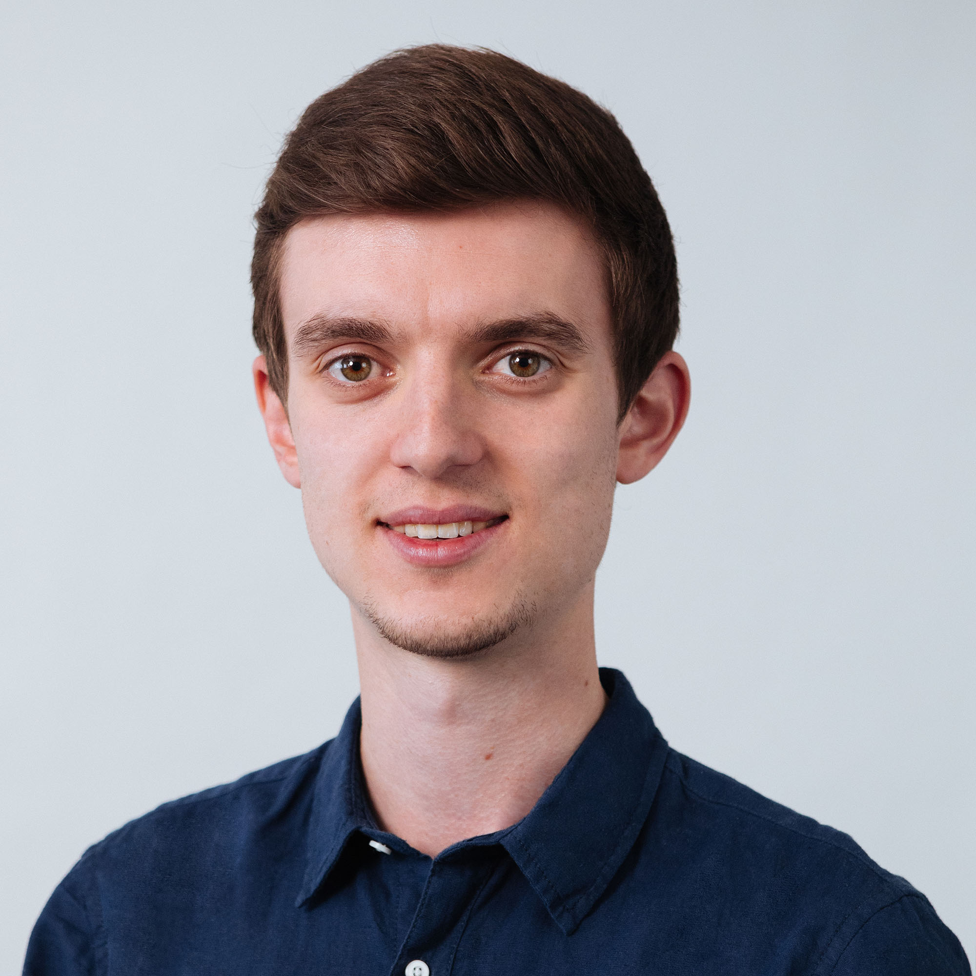 Eine Person mit braunen Haaren in einem dunkelblauen Hemd vor hellem Hintergrund.